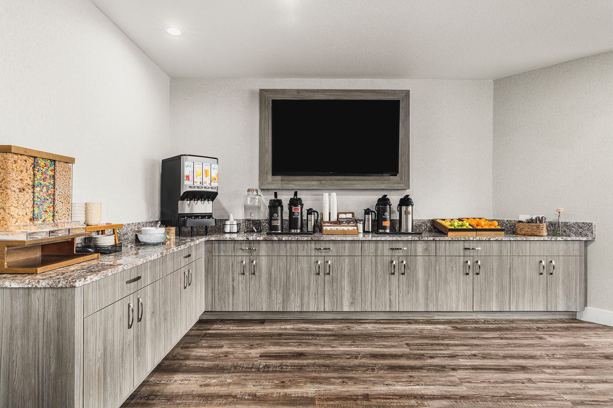 A modern kitchen with a built-in TV, coffee maker, and fruit display.