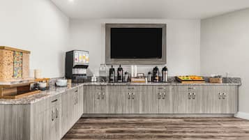 A modern kitchen with a built-in TV, coffee maker, and fruit display.