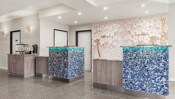 A reception area with three counters, each with a unique mosaic tile design. There are wooden cabinets to the left and a wall with a floral pattern to the right.