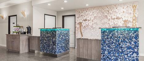 A reception area with three counters, each with a unique mosaic tile design. There are wooden cabinets to the left and a wall with a floral pattern to the right.