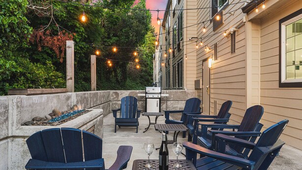 An outdoor patio with Adirondack chairs, a grill, and string lights. - The Ashley Inn & Suites (Lincoln City)