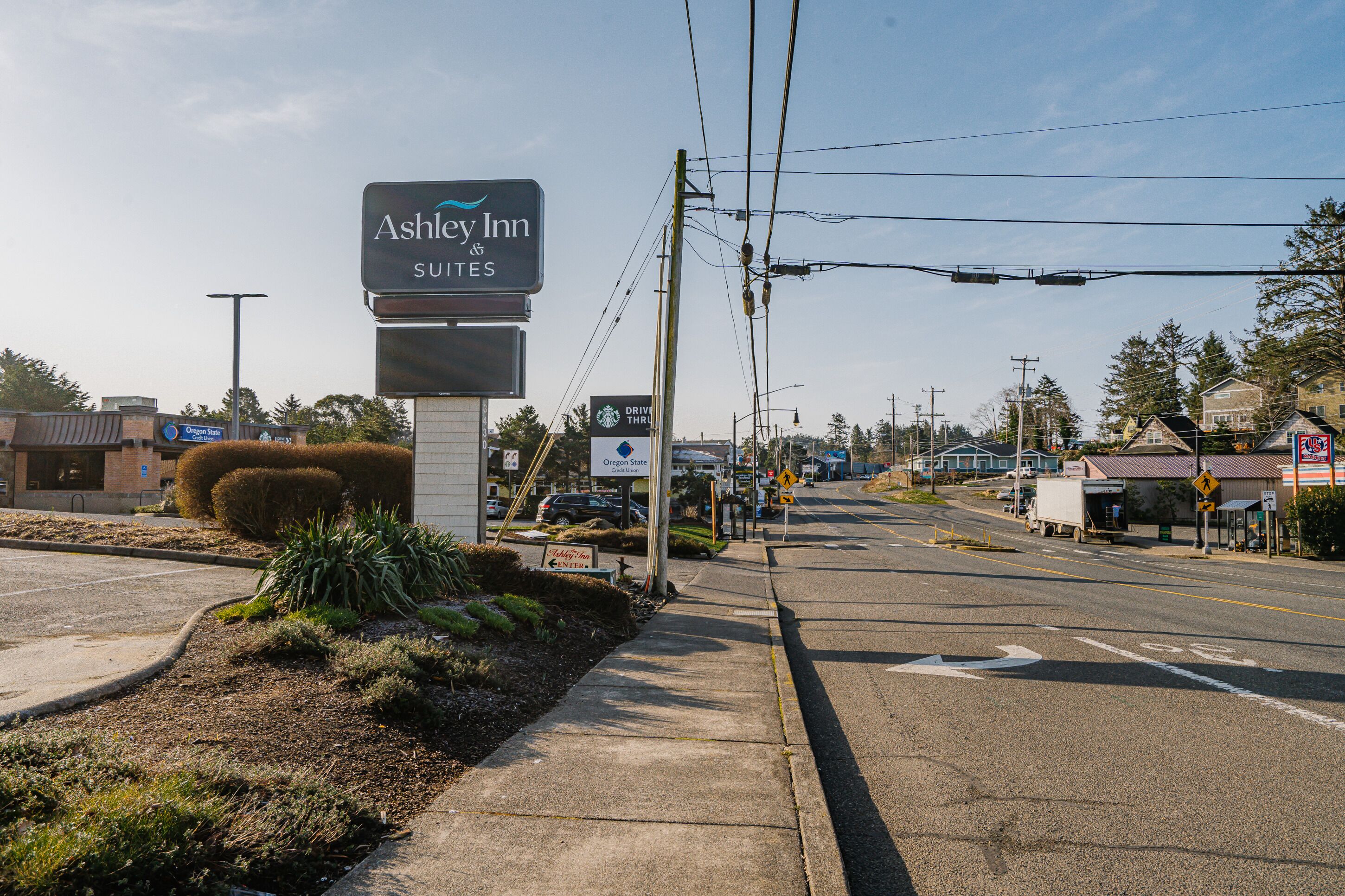 Une route menant à un hôtel appelé Ashley Inn Suites, avec un ciel dégagé et quelques bâtiments visibles au loin.