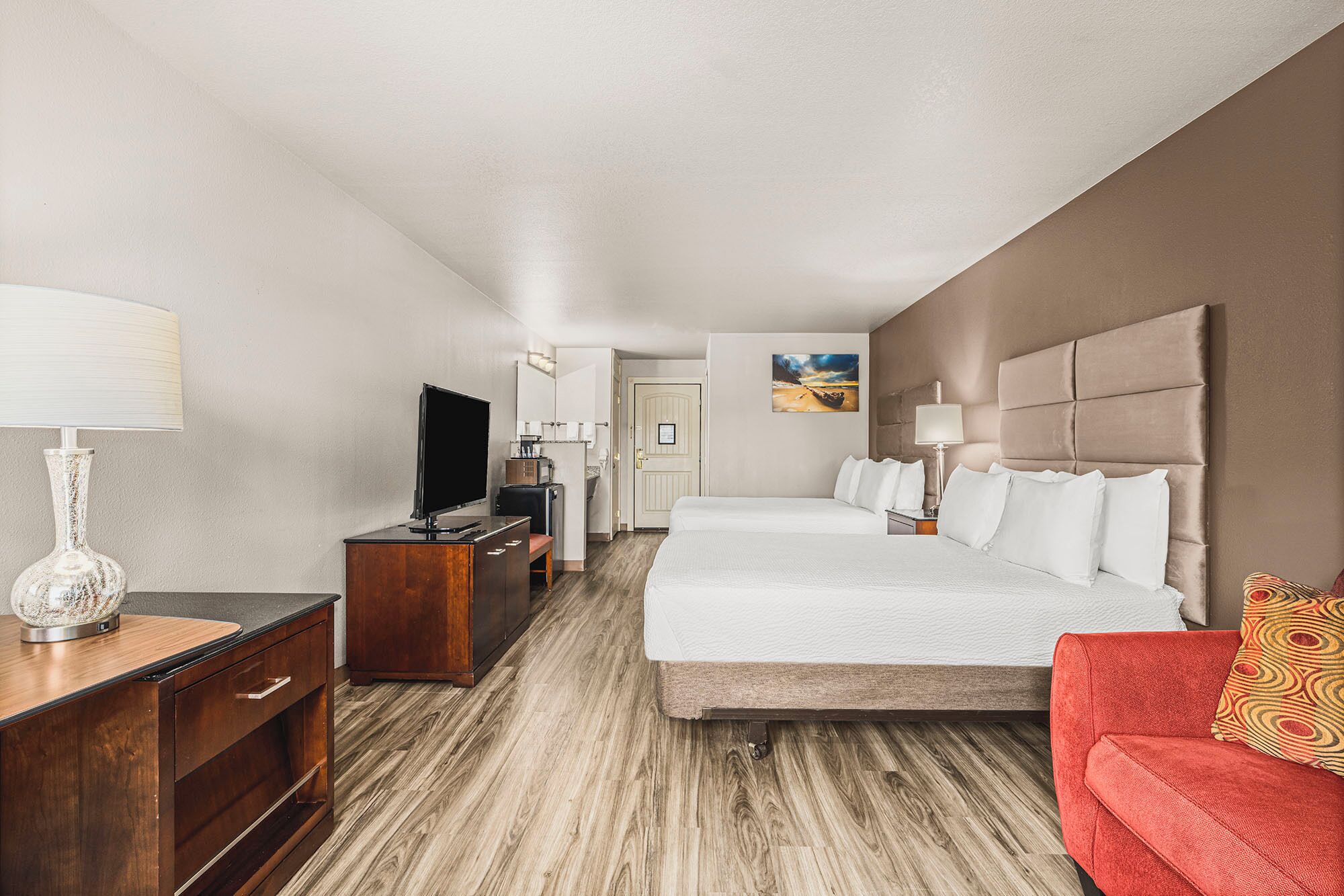 Una habitación de hotel con una cama grande, un escritorio con lámpara, una televisión y una silla roja.