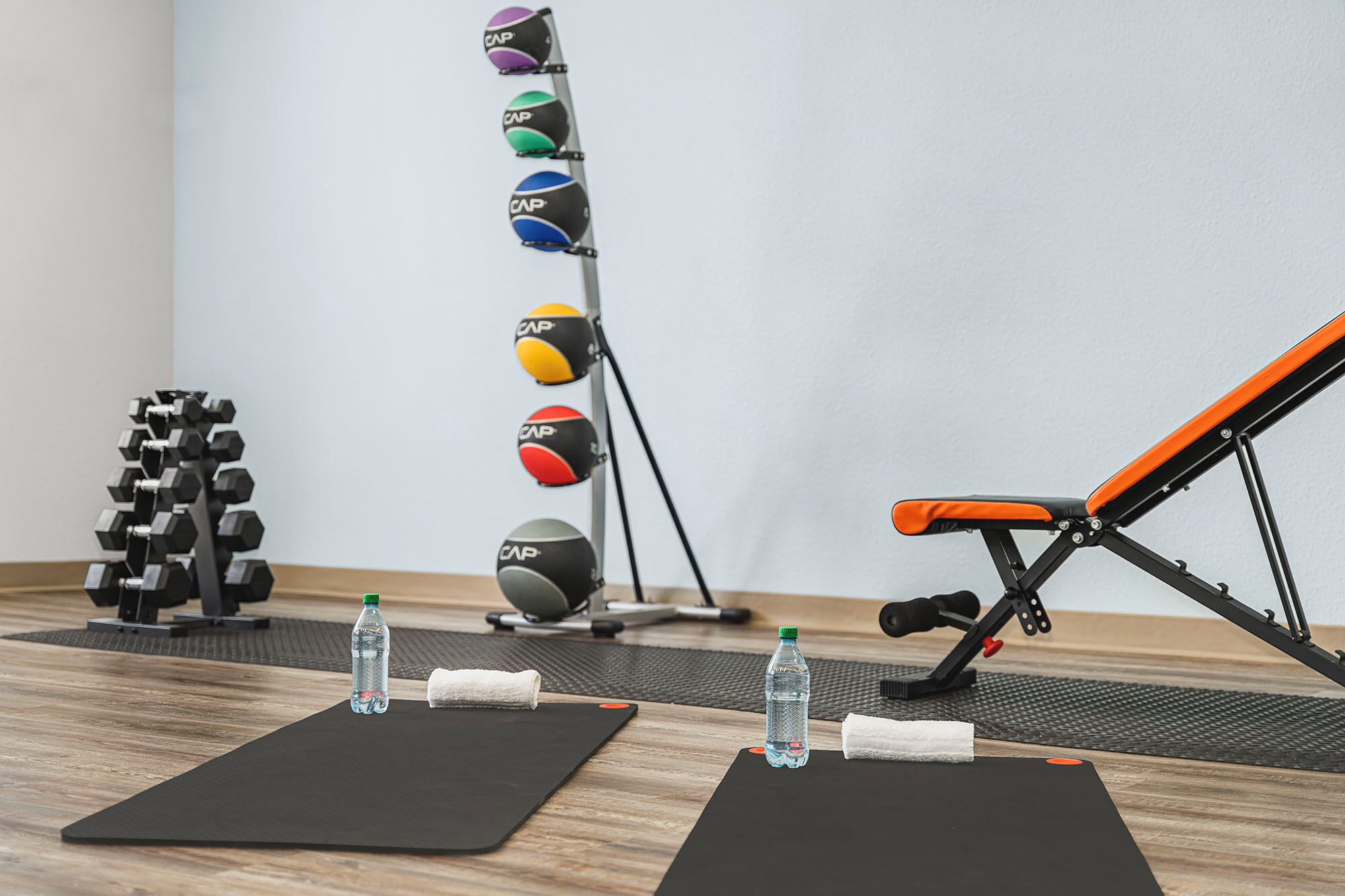 Une salle de sport équipée de matériel d’exercice, de tapis noirs, d’haltères et de bouteilles d’eau.
