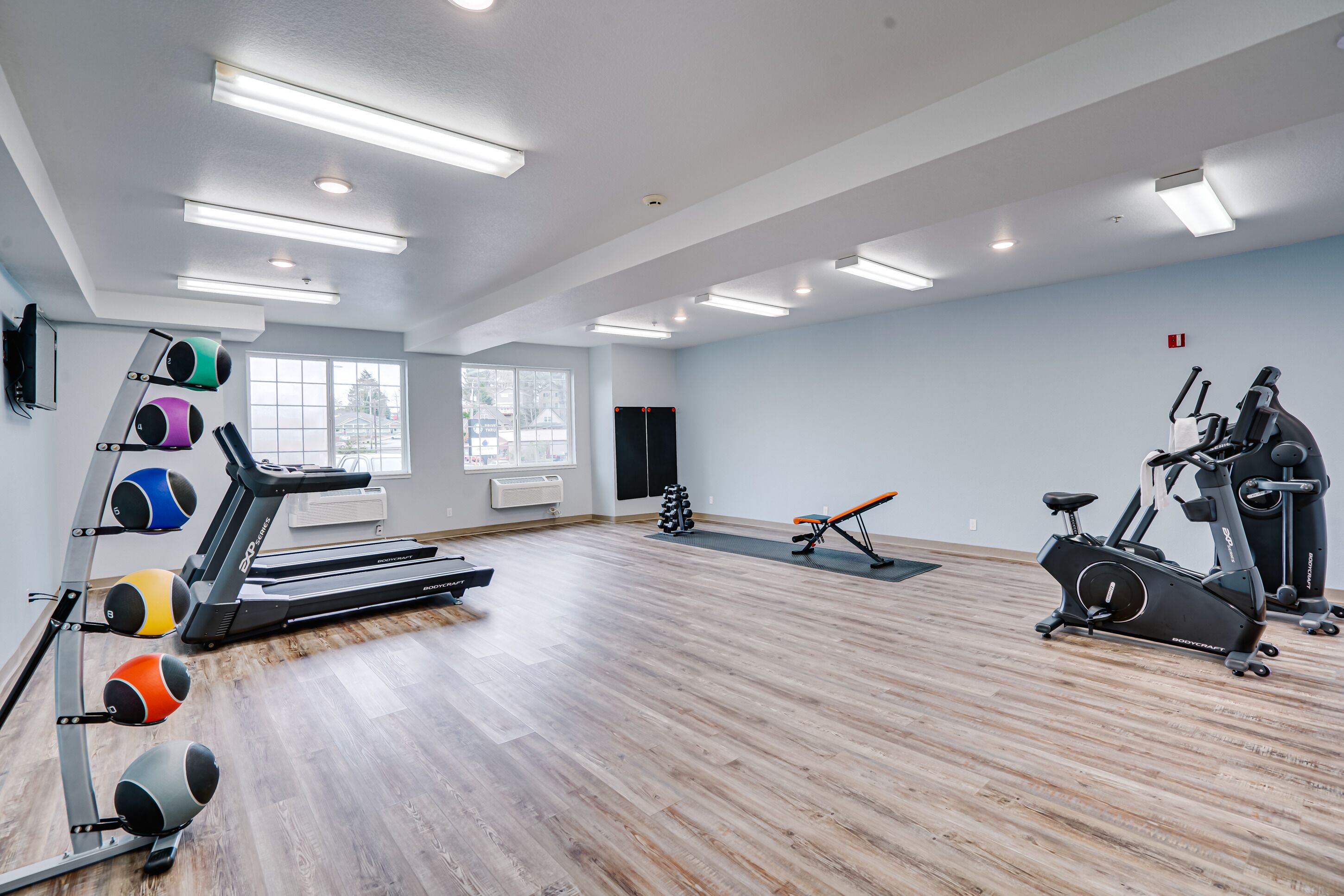Un gimnasio espacioso con piso de madera, caminadoras, una elíptica y una máquina de remo.