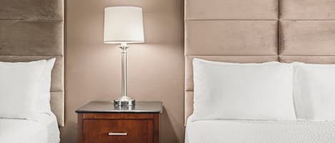 A hotel room with two beds, a nightstand with a lamp, and a wooden dresser.