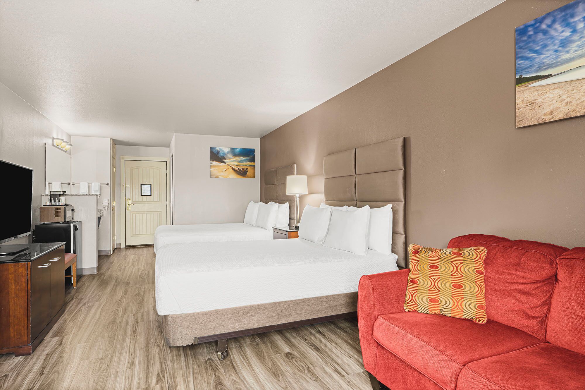 A hotel room with a large bed, a red sofa, a television, and a painting on the wall.