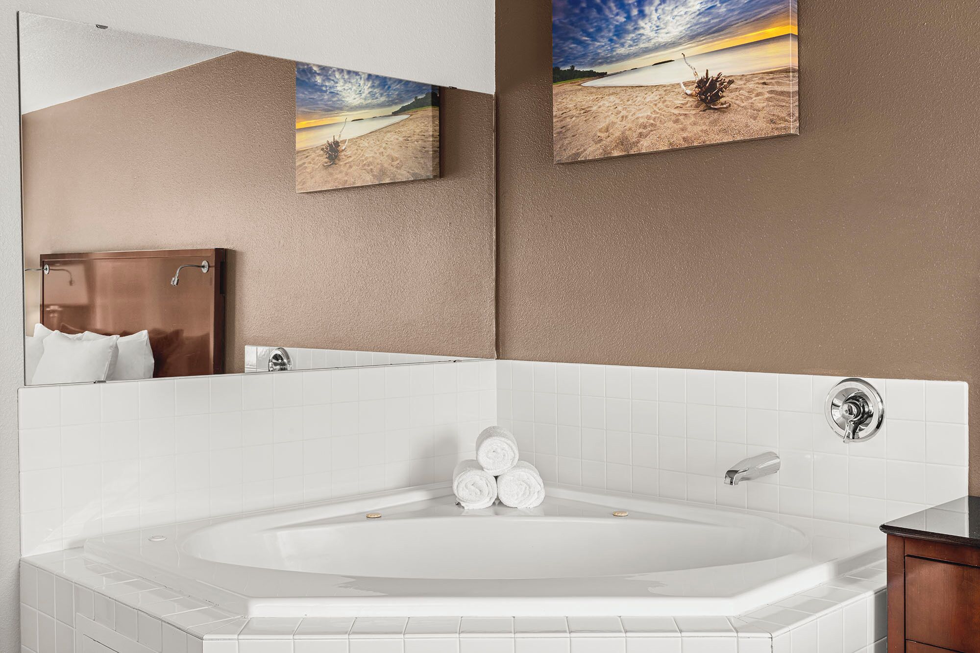 A modern bathroom with a large bathtub, white tiles, and two framed pictures of a beach scene.
