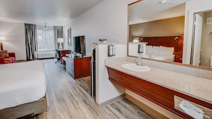 A hotel room with a bed, a desk, a television, a minibar, a large mirror, and a bathroom with a sink and toilet. - The Ashley Inn & Suites (Lincoln City)