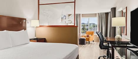 A hotel room with a large bed, a desk with a chair, a television, and a window with curtains.