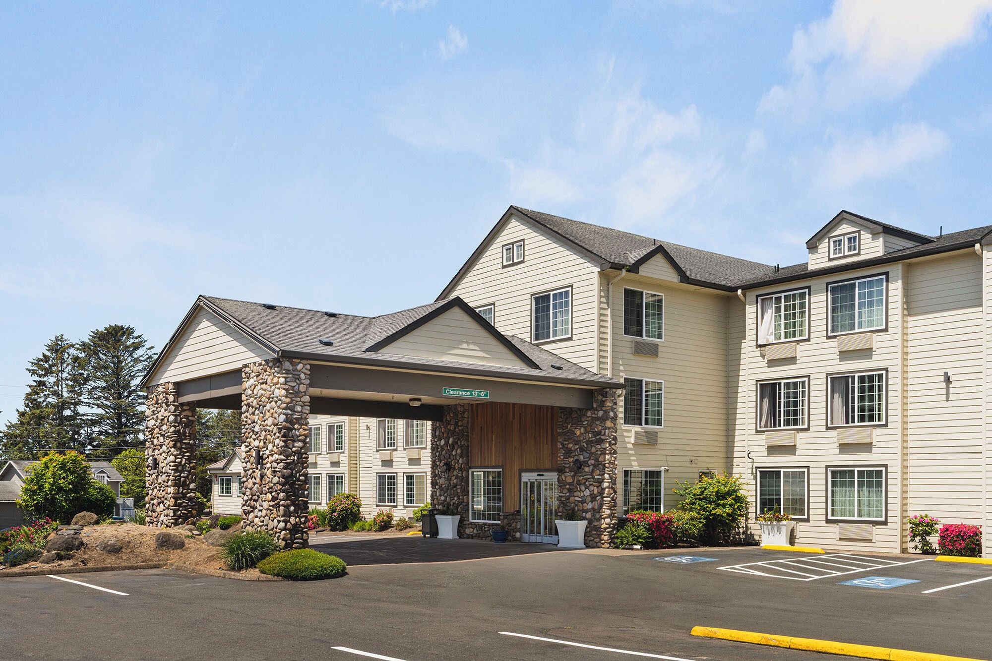 A multi-story hotel with a stone facade, a covered entrance, and a parking lot with handicapped parking.