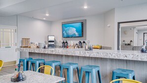 A modern bar area with a large TV screen, bar stools, and a marble countertop. - The Ashley Inn & Suites (Lincoln City)