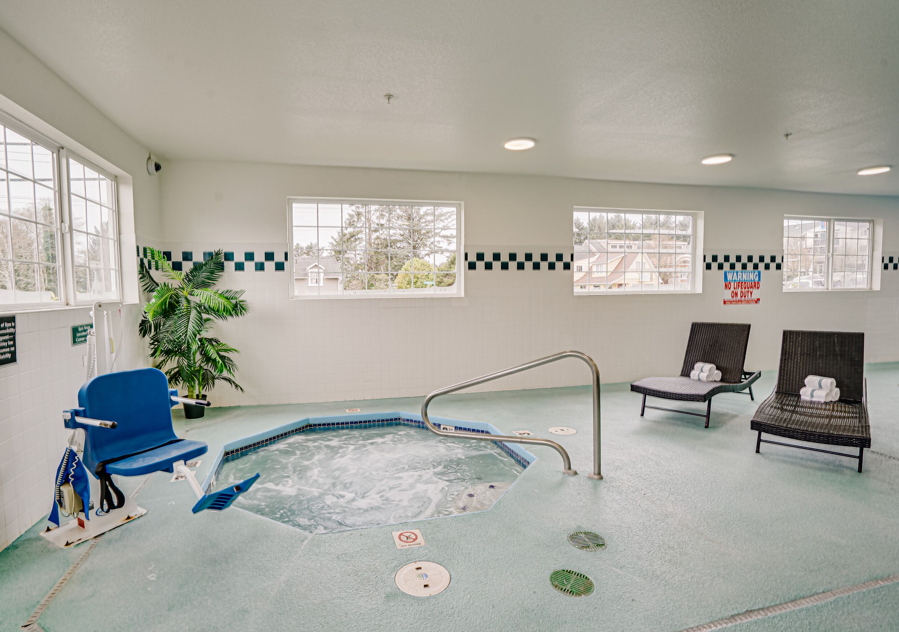 An indoor pool area with a hot tub, lounge chairs, and a potted plant.