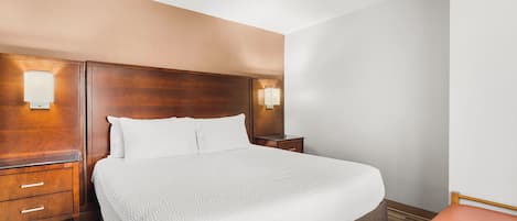 A hotel room with a large bed, wooden headboard, two bedside tables with lamps, a wooden nightstand, and a wooden chair.