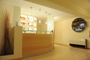 A reception area with a curved counter, hanging pendant lights, a mounted TV, and a wall-mounted shelf with various items. - Pizzomunno Vieste Palace Hotel (Vieste)
