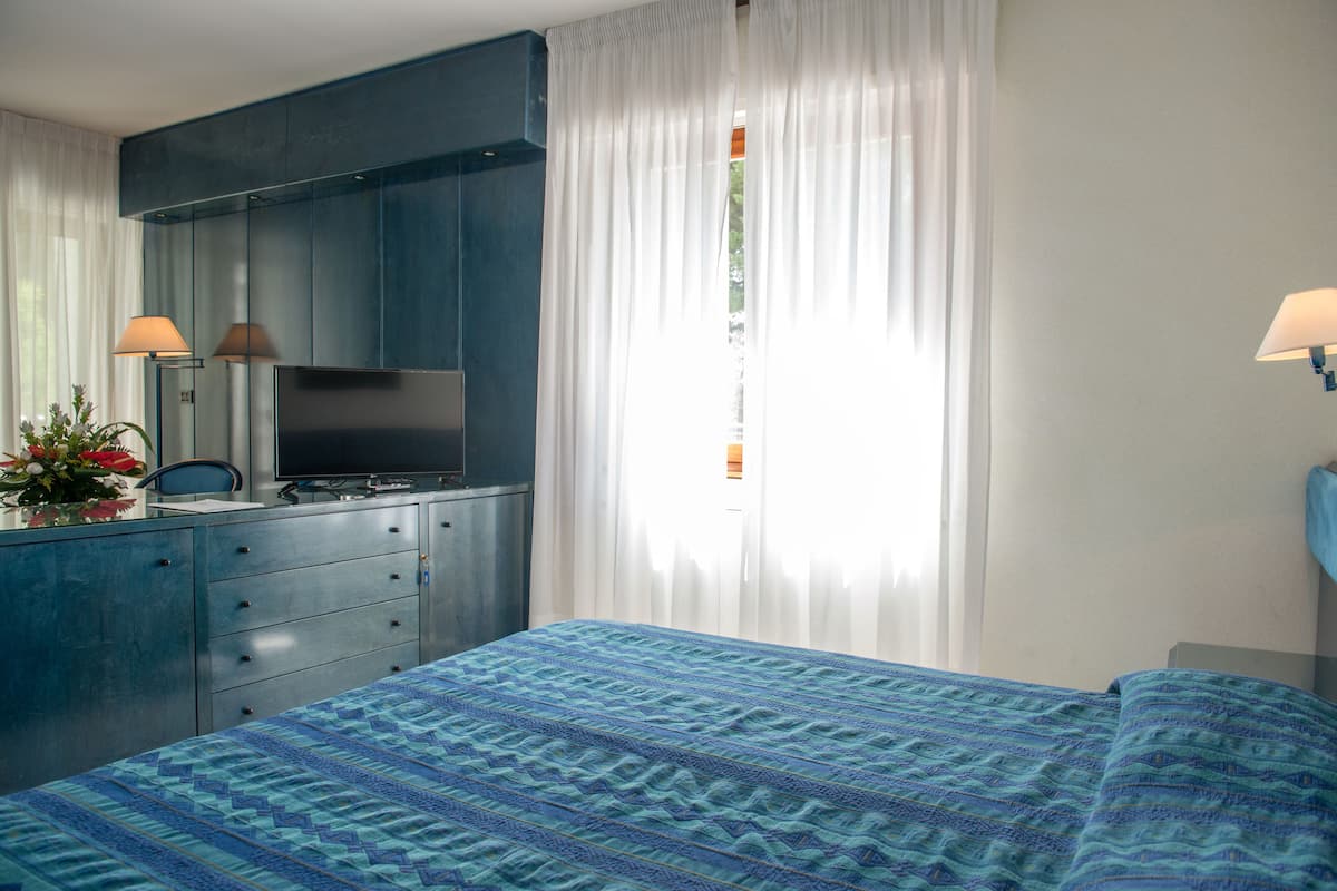 Ein Schlafzimmer mit Bett, Kommode, Fernseher und einem Fenster mit Vorhängen.
