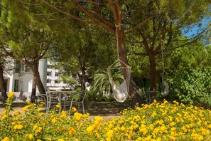 A hammock hanging from a tree, surrounded by yellow flowers and a metal table with chairs. - Pizzomunno Vieste Palace Hotel (Vieste)