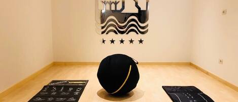 A room with a wooden floor, a black exercise ball, and two black mats with illustrations.