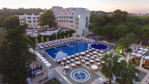 Relax by the pool surrounded by lush greenery and modern hotel buildings with spacious balconies.