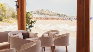 Un espace aménagé avec des sièges, situé au bord de la plage, d’où l’on peut admirer la plage et une colline en arrière-plan.