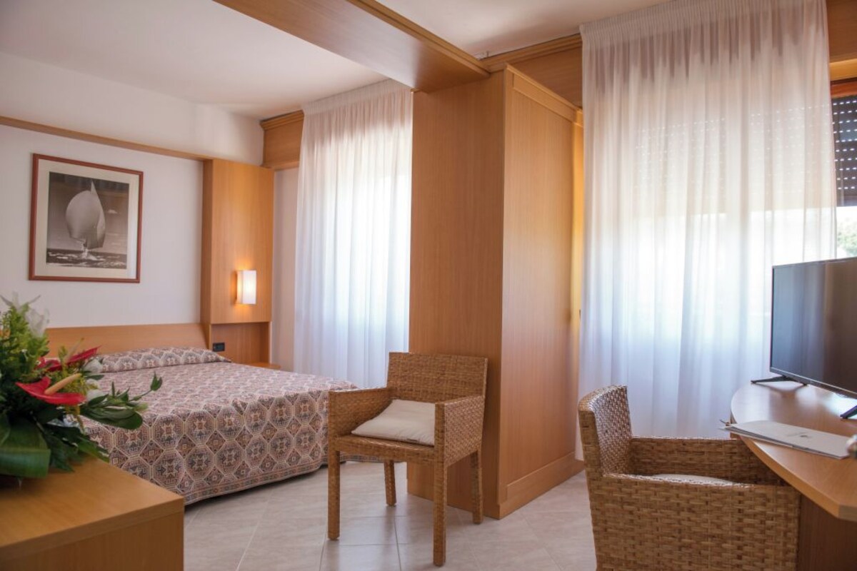 Une chambre d’hôtel avec un lit, un bureau avec un ordinateur portable, une chaise, une télévision et un tableau encadré au mur.