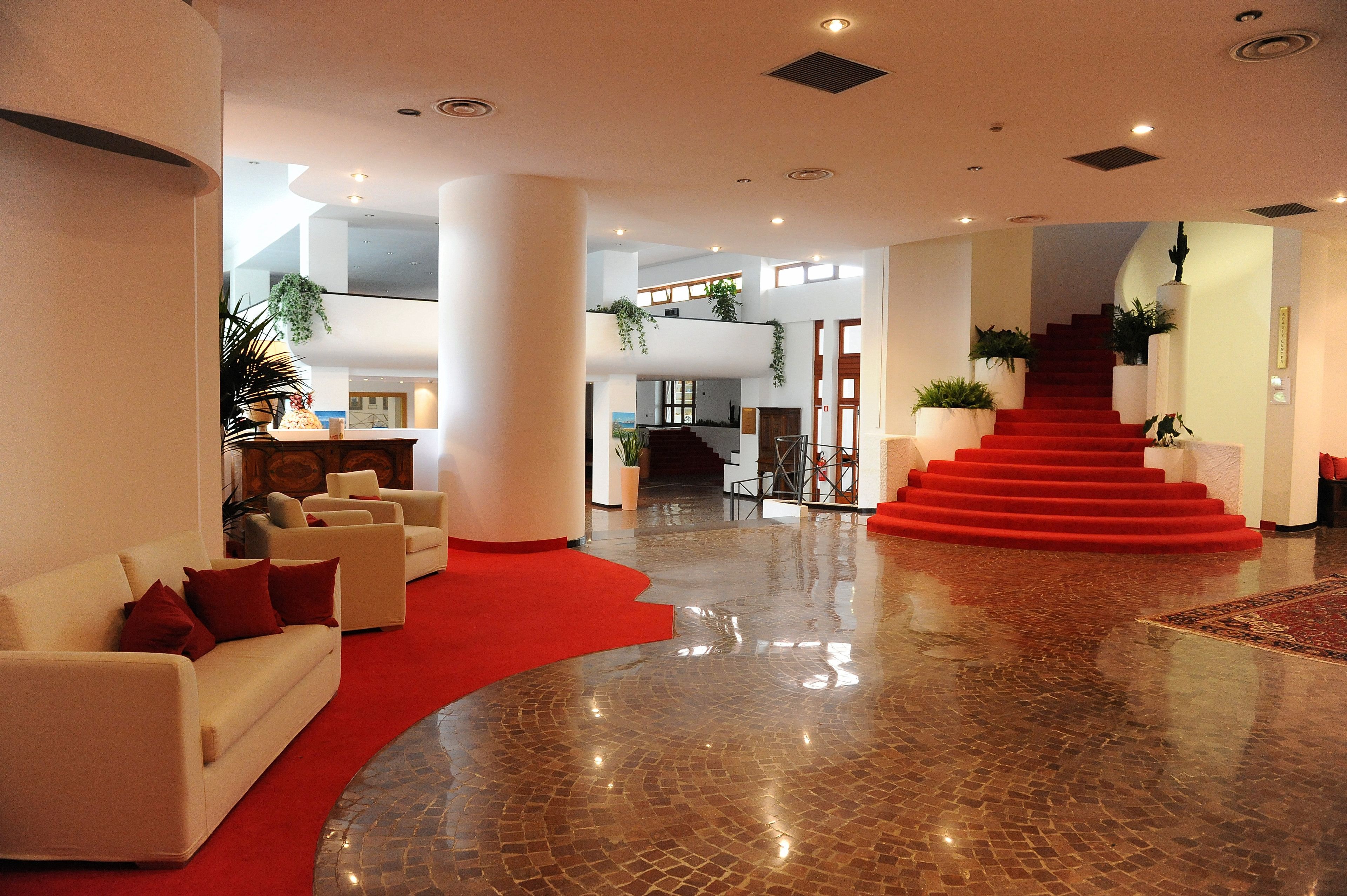 Un hall d’entrée spacieux, doté d’un tapis rouge, d’un escalier et d’un plafond haut avec des luminaires encastrés.