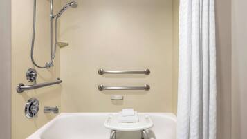 A bathroom with a bathtub, a shower with a handheld showerhead, grab bars, and a towel rack.