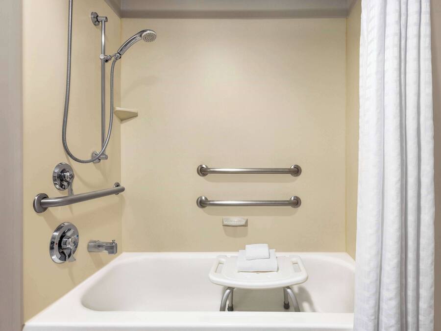 A bathroom with a bathtub, a shower with a handheld showerhead, grab bars, and a towel rack.