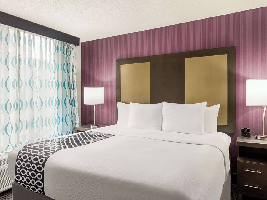 A hotel room with a large bed, two bedside tables with lamps, a headboard, and a window with curtains.