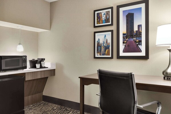 Une chambre d’hôtel équipée d’une kitchenette, d’un bureau, d’une chaise et de tableaux représentant des vues de la ville, accrochés au mur.
