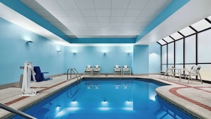 Una piscina con revestimiento azul, rodeada de sillas de descanso y un área de vestuarios.