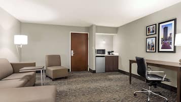 A hotel room with a sofa, armchair, desk, and kitchenette.