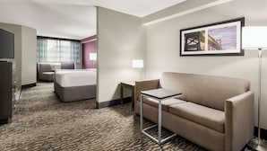 Habitación de hotel con cama, sofá, una mesita, televisor y un cuadro en la pared.