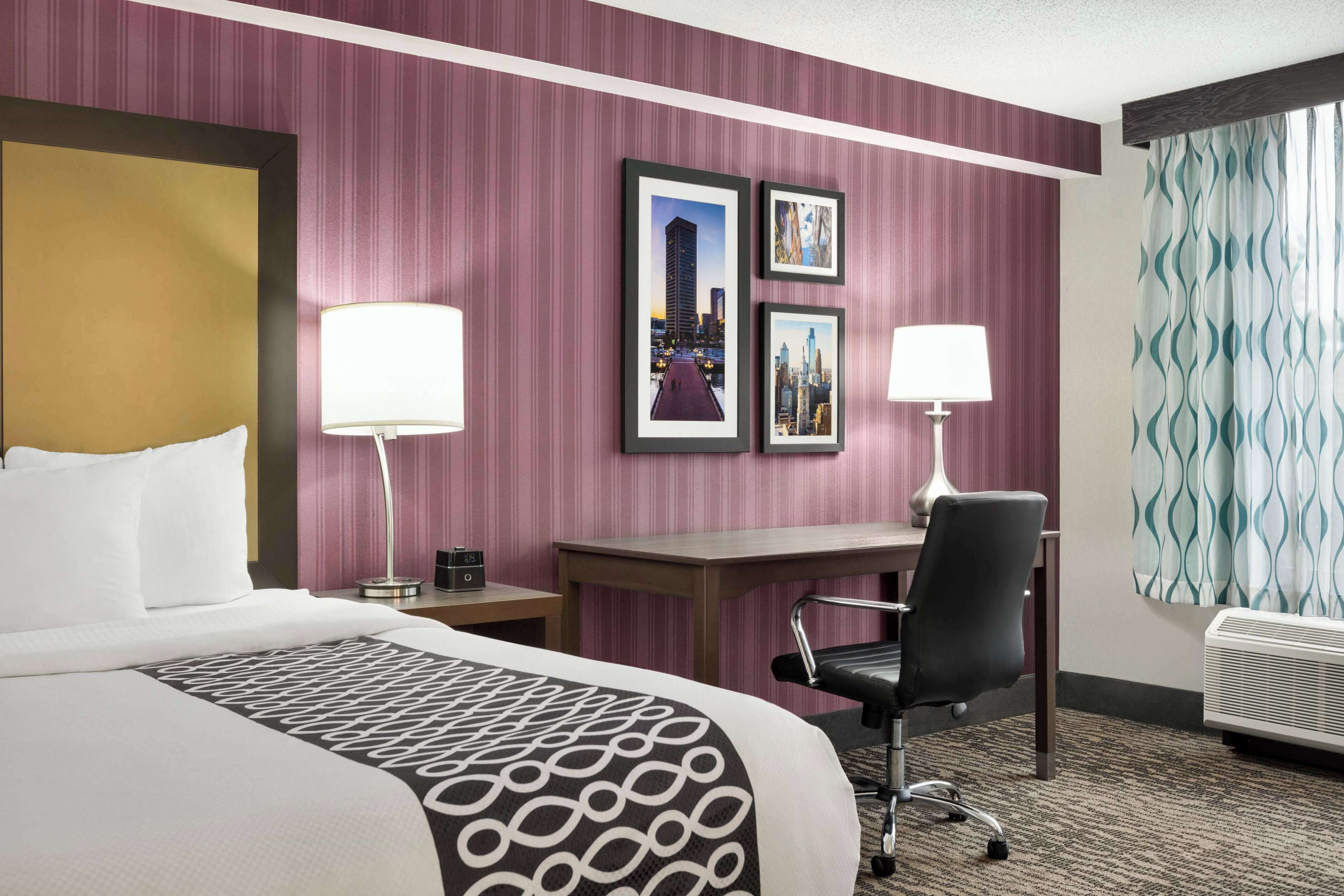 A hotel room with a large bed, a desk, two chairs, a lamp, and framed pictures on the wall.