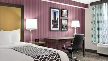 A hotel room with a large bed, a desk, two chairs, a lamp, and framed pictures on the wall.