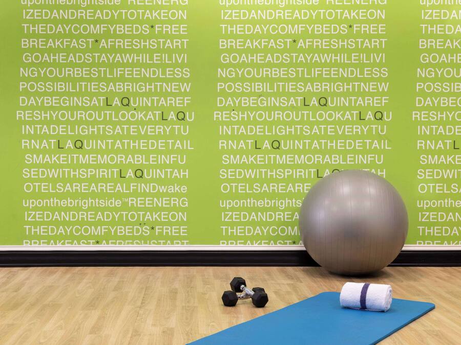 Un gimnasio con equipo de ejercicio, una colchoneta de yoga y frases motivacionales en la pared.