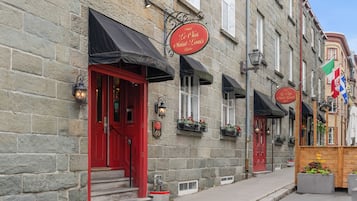 A stone building with a red door and black awning, featuring a sign for 'Le Clovis Saint-Louis'.