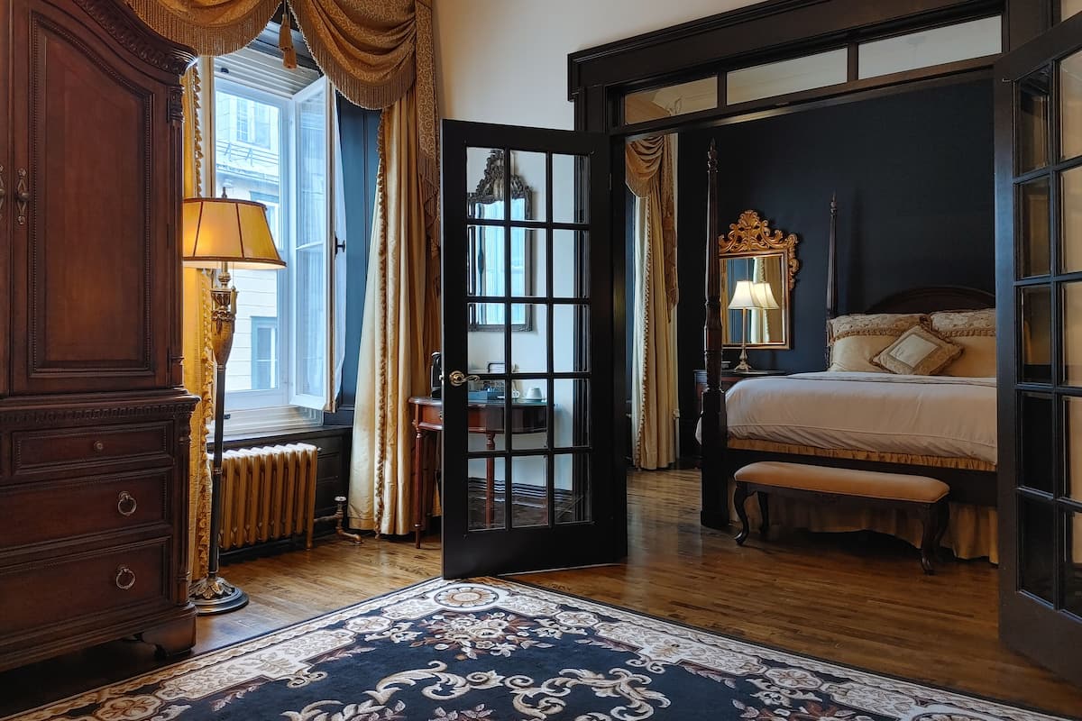 Un dormitorio tradicional con cama con dosel, un espejo grande y un aparador de madera.