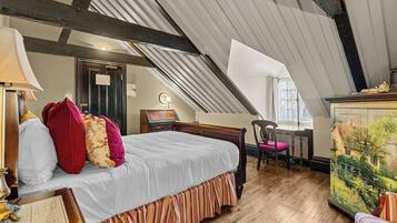 A bedroom with a sloped ceiling, a bed with a striped skirt, a desk with a chair, and a painting of a house.
