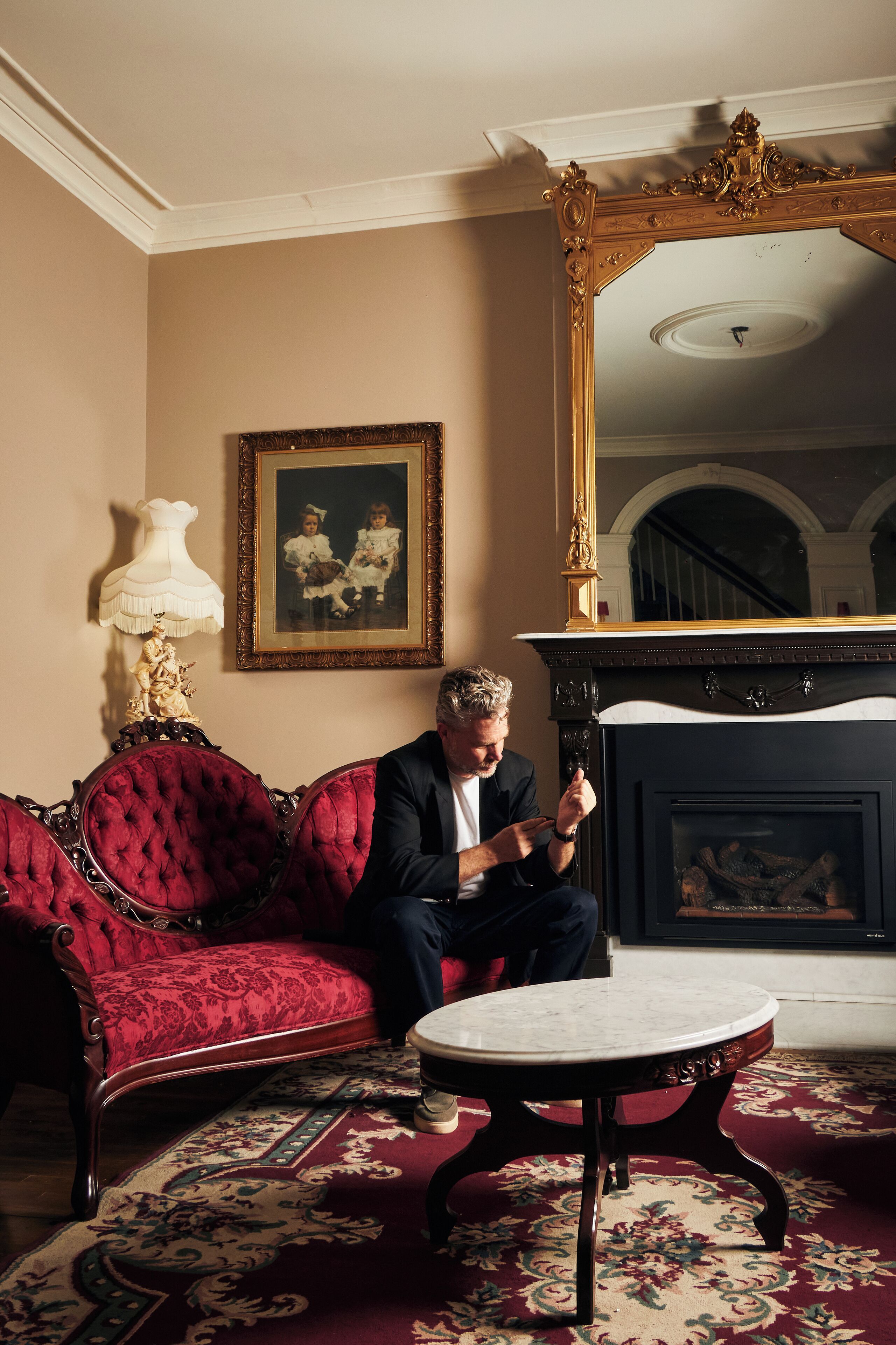 A room with a red upholstered sofa, a round table, a large ornate mirror, and a framed picture on the wall.