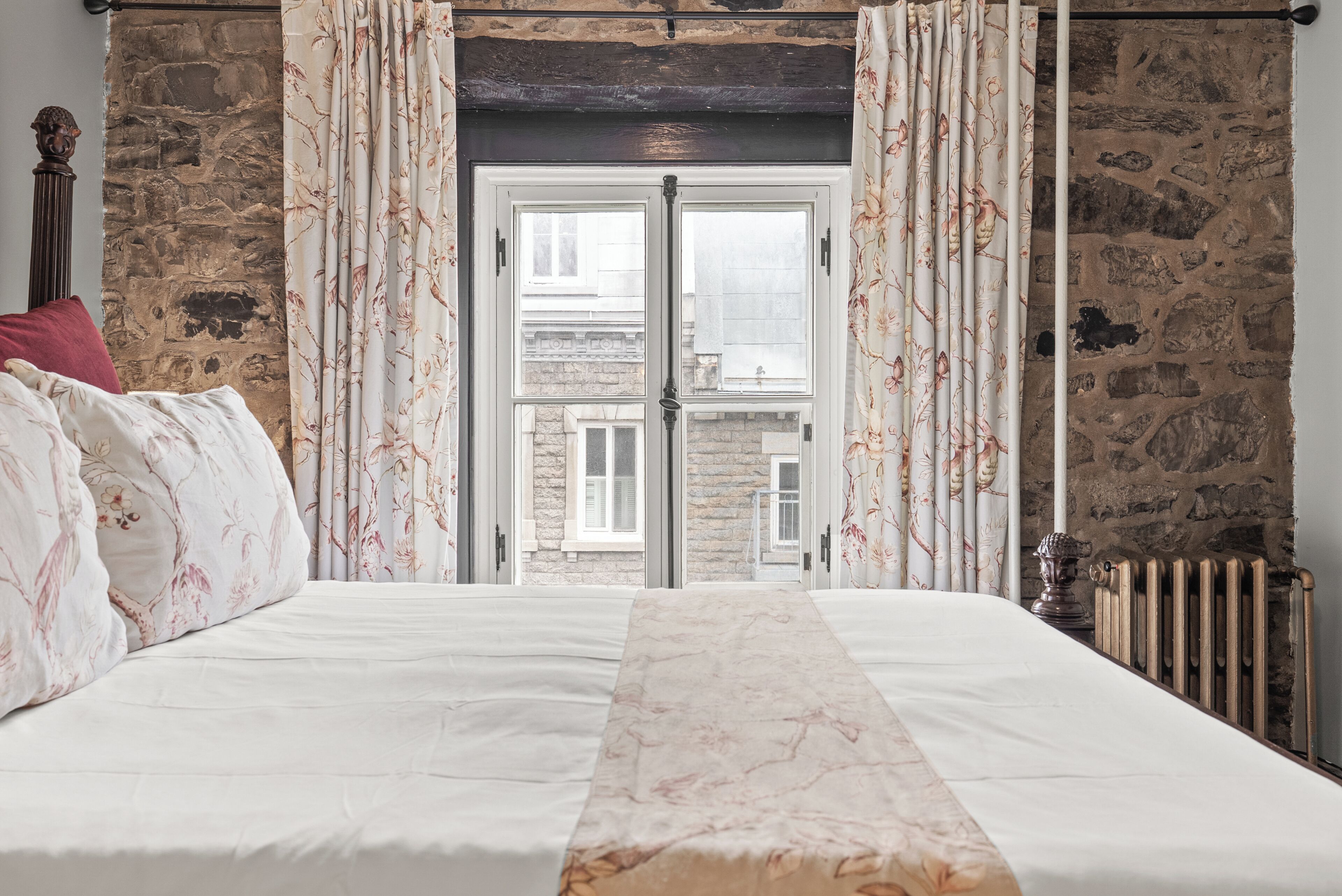A bedroom with a bed, stone walls, a window, and a radiator.