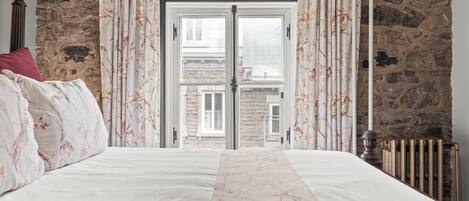 A bedroom with a bed, stone walls, a window, and a radiator.