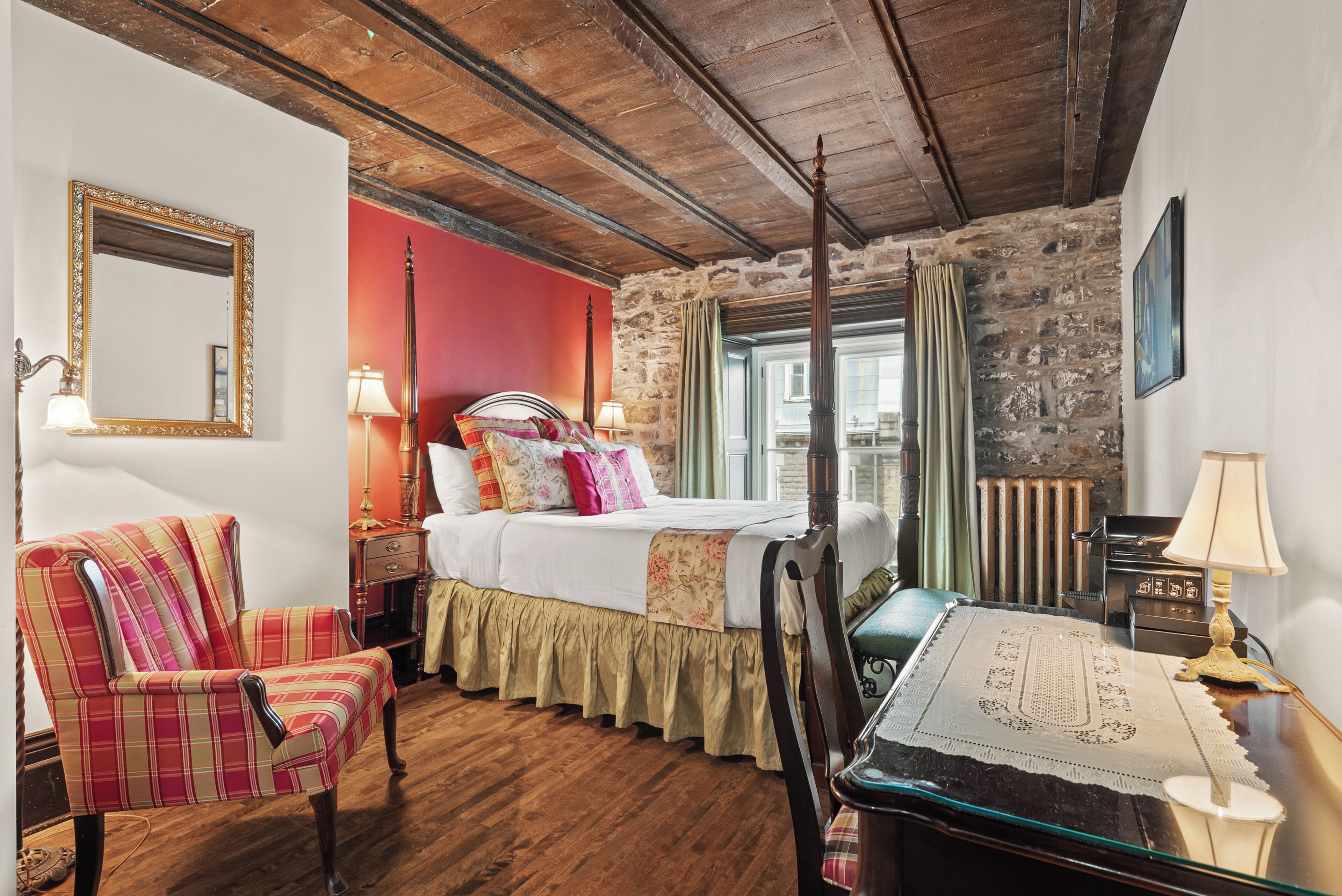 A room with a bed, a chair, a table, and a mirror.