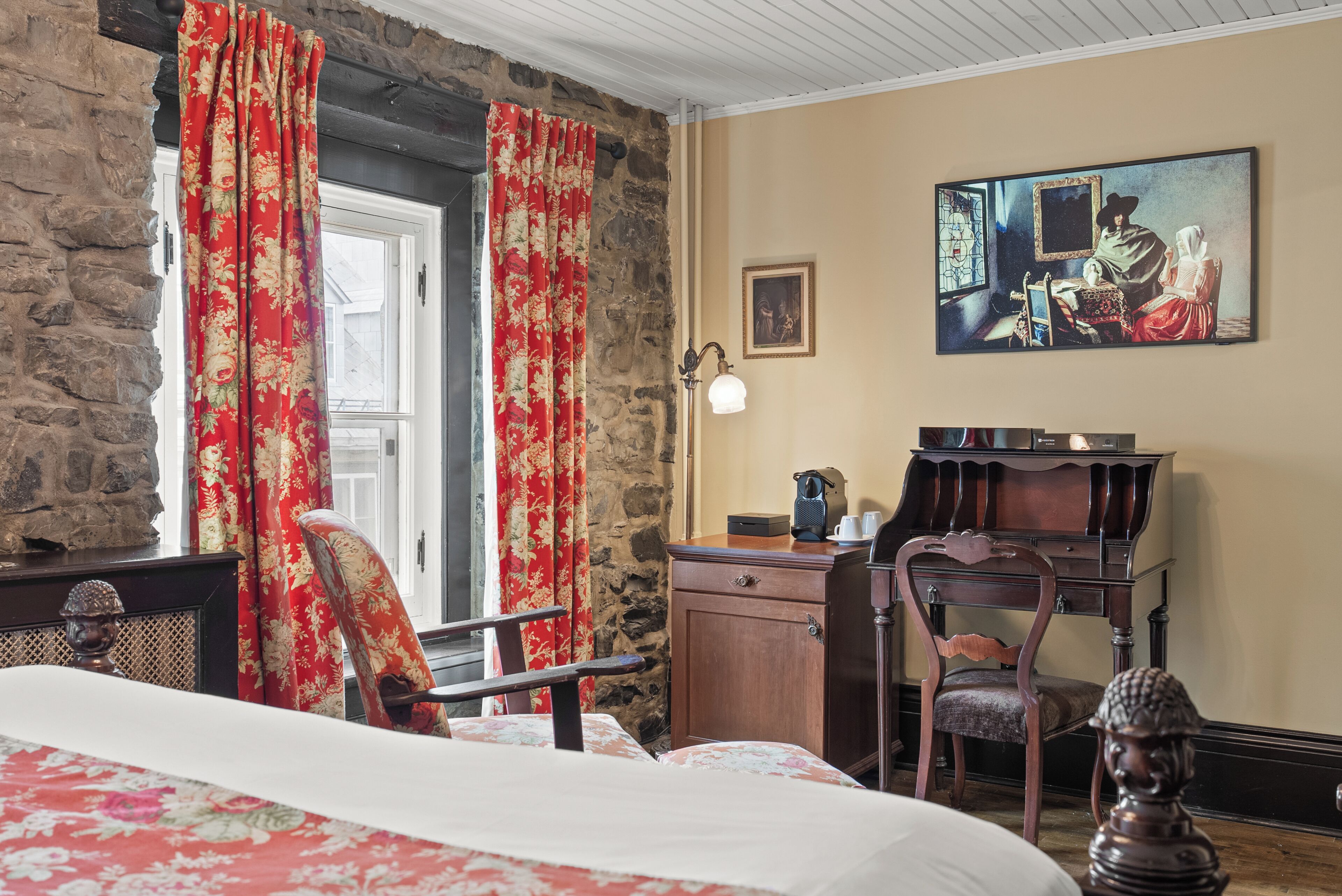 A room with a bed, a desk, a chair, a lamp, and a painting on the wall.