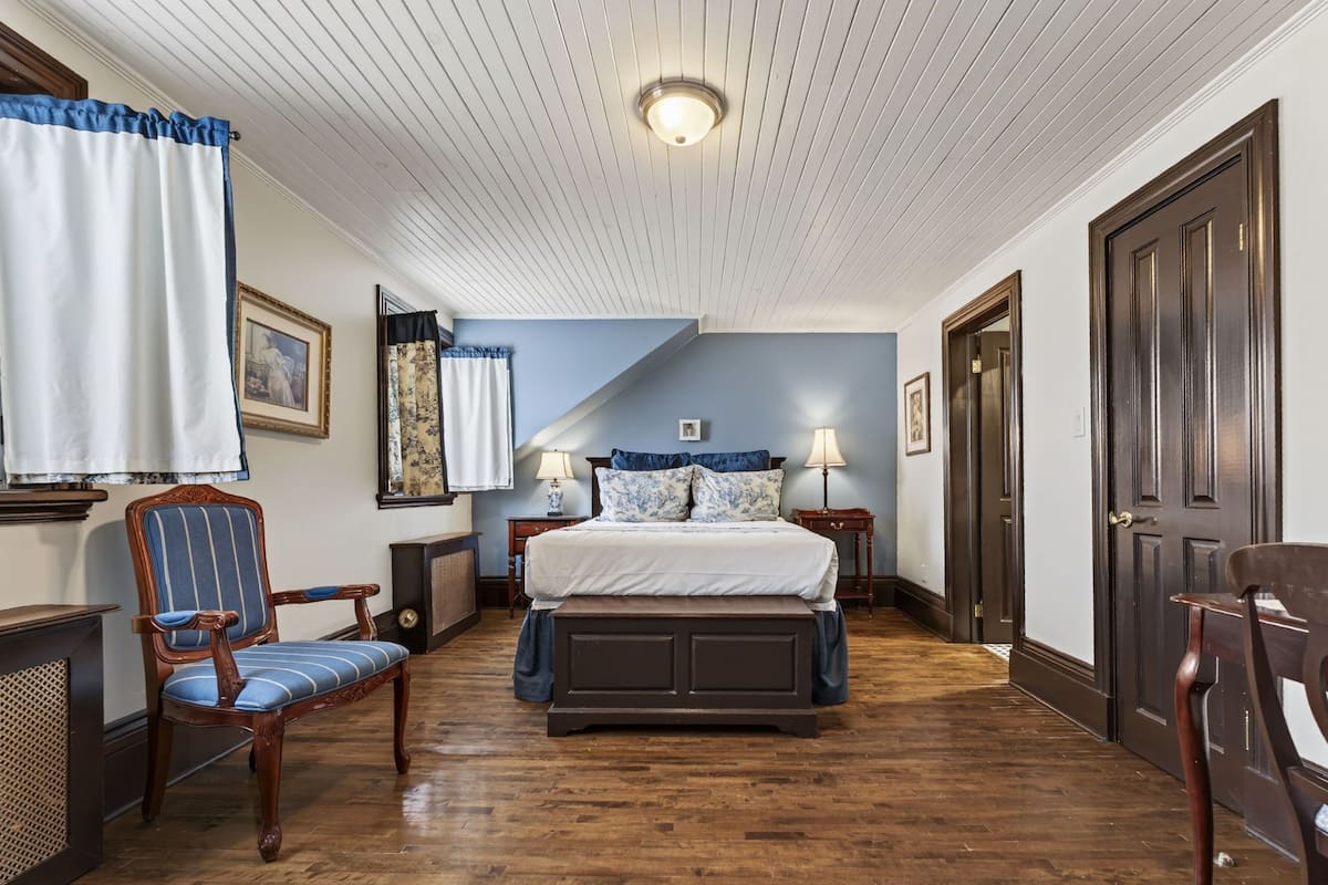 Un dormitorio con cama, una silla, cómoda, mesita de noche y una puerta.