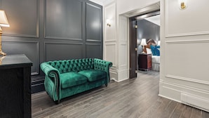 Una habitación con un sofá de terciopelo verde oscuro, una mesita de madera y una lámpara.