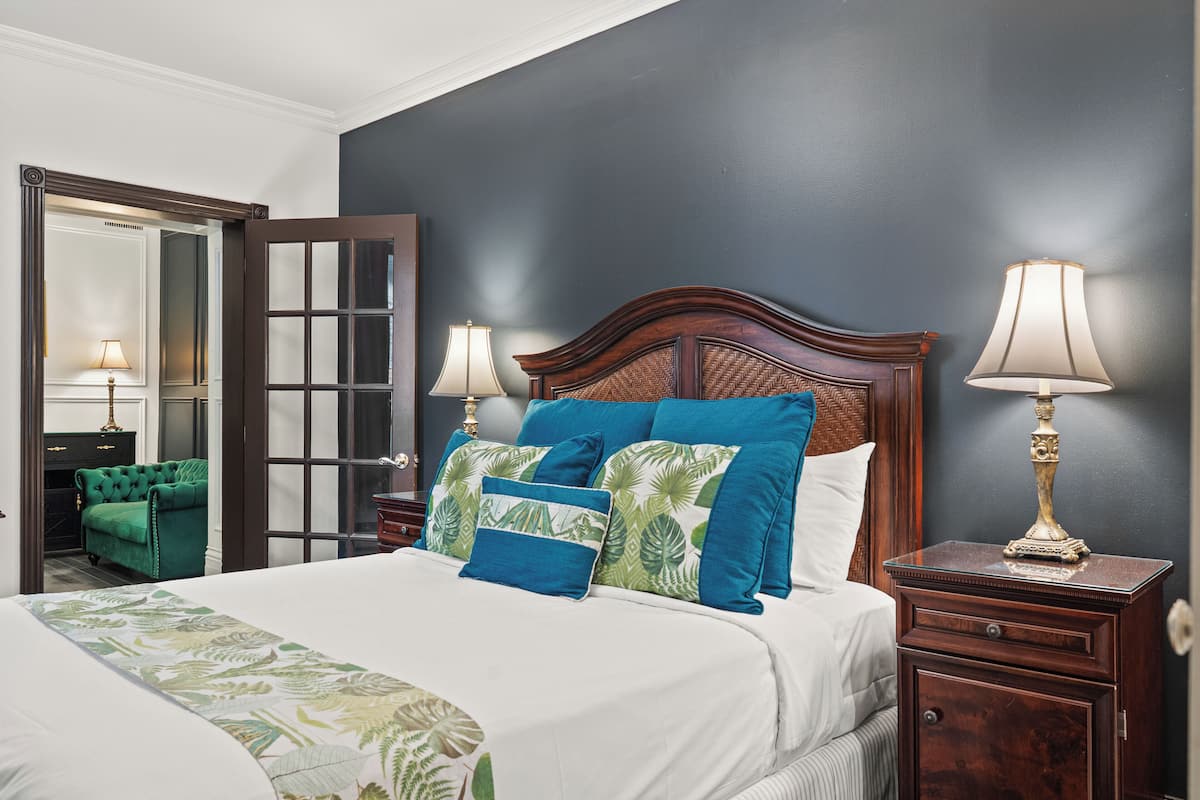 Una habitación de hotel con una cama grande, dos lámparas de noche, un sillón verde y una mesita de noche de madera.