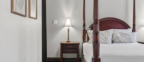 Una cama con dosel y tablero de madera, una mesita de noche con lámpara y cuadros enmarcados en la pared.