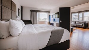 A modern hotel room with a large bed, a desk, a sofa, and a city view. - Hôtel Le Dauphin Montréal - Longueuil (Longueuil)