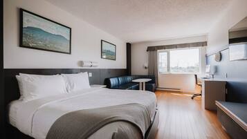 A hotel room with a large bed, a desk, a chair, a small round table, and a television.